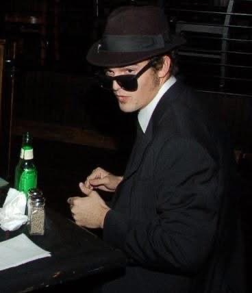 Robert Vicens in a black suit, fedora, and sunglasses backstage