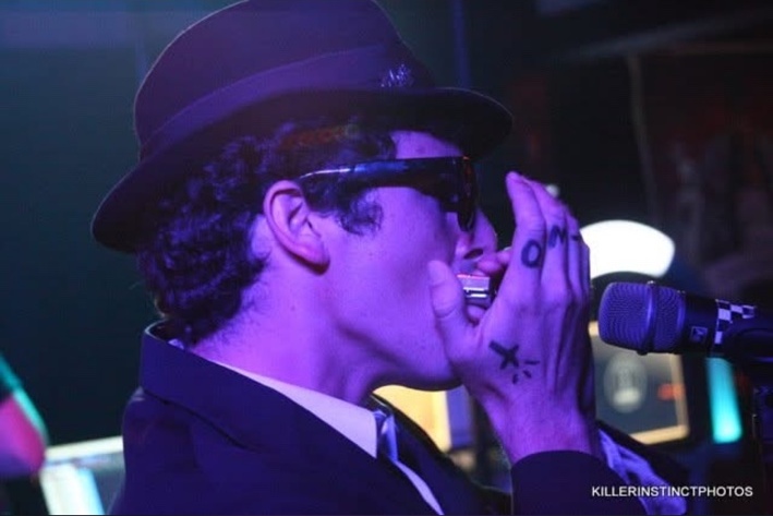Robert Vicens playing harmonica into a stage microphone under purple light